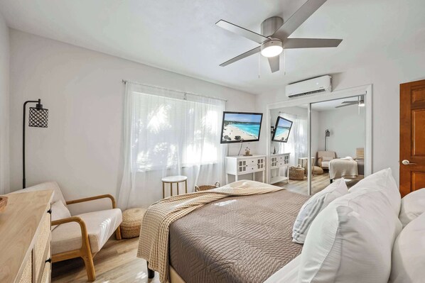 Une chambre à coucher avec un lit, un ventilateur de plafond, une télévision et un miroir.