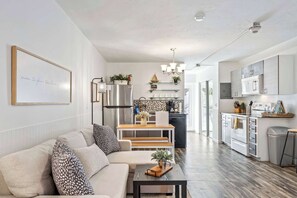 Una cocina moderna con electrodomésticos de acero inoxidable, un comedor con mesa y banco de madera, y una sala de estar con sofá y mesa de centro.