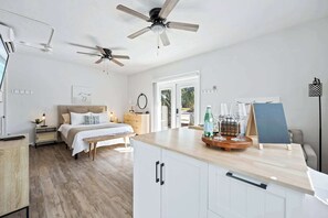 A bedroom with a bed, bedside tables, a nightstand, a ceiling fan, and a window. - Sandpiper Studio | Across From Beach! (Satellite Beach)