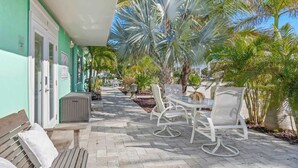 A patio area with a table and chairs, a bench, and a pathway lined with palm trees. - Sandpiper Studio | Across From Beach! (Satellite Beach)