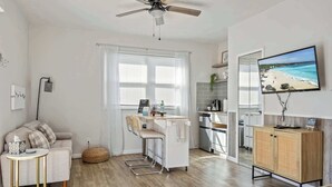 A modern living room with a sofa, a small round table, a bar area, a television, and a kitchen in the background. - Sandpiper Studio | Across From Beach! (Satellite Beach)