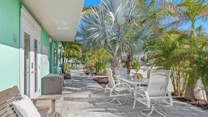 A patio with outdoor seating, palm trees, and a building with a green facade.