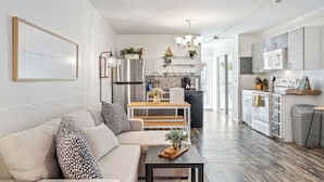 A modern kitchen with stainless steel appliances, a dining area with a wooden table and bench, and a living room with a sofa and coffee table.