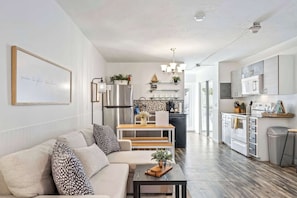 Una cocina moderna con electrodomésticos de acero inoxidable, un comedor con mesa y banco de madera, y una sala de estar con sofá y mesa de centro.