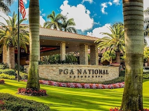 Entrée du PGA National Resort & Spa, avec sa façade en pierre, ses palmiers et un ciel d’un bleu éclatant.