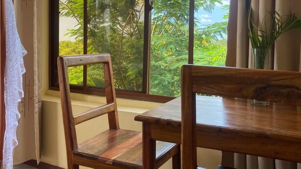 A room with a large window, wooden furniture, and a view of trees. - Authentic Mikoko Beach & Cottages (Bagamoyo)