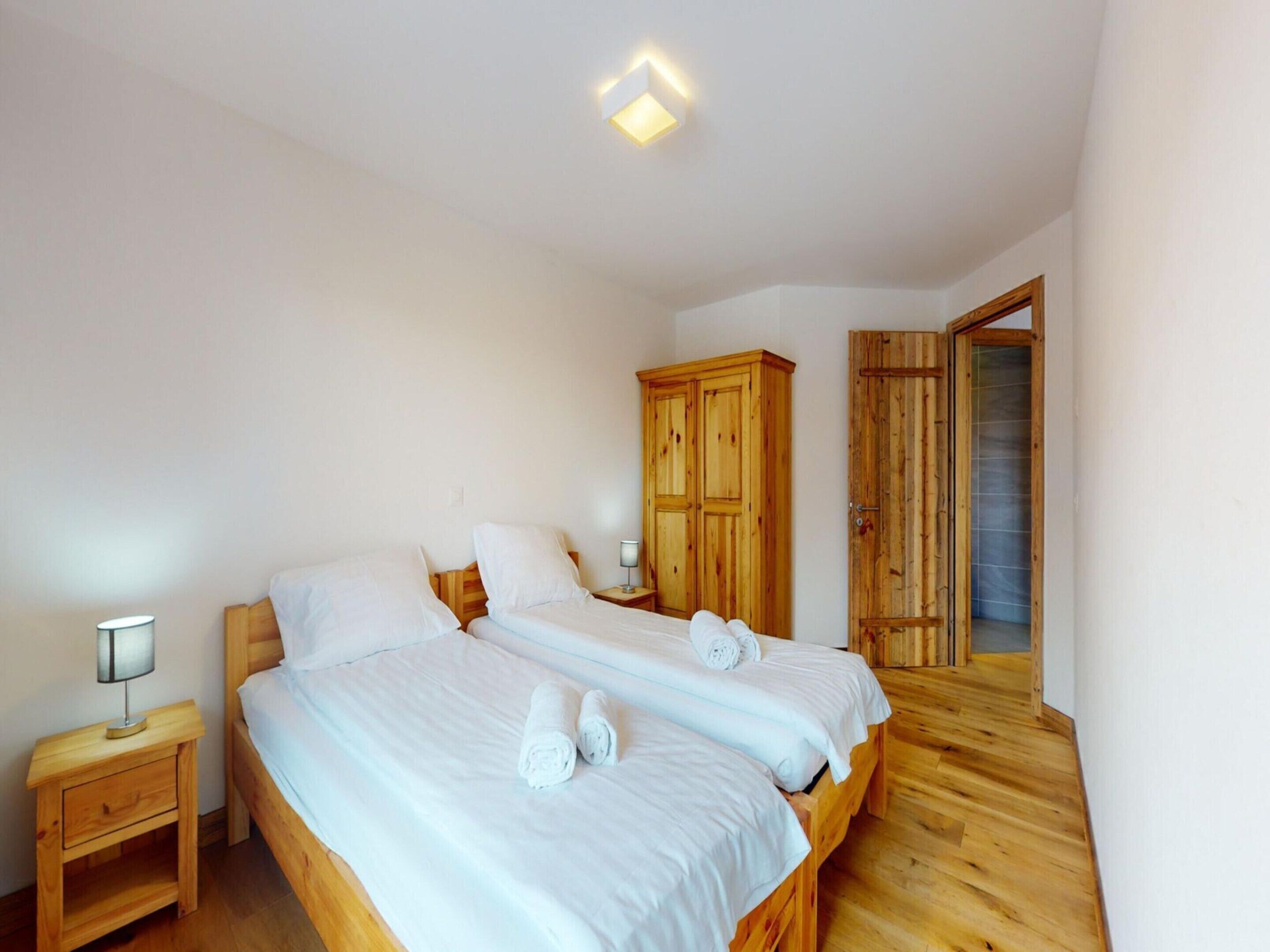 A bedroom with two single beds, wooden wardrobes, a nightstand with a lamp, and a wooden floor.
