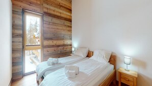 A bedroom with two beds, wooden ceiling, and a window. - Apartment in Ski In Ski Out Location (Veysonnaz)