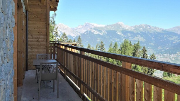 A wooden balcony with a table and chairs, overlooking a mountainous landscape. - Apartment in Ski In Ski Out Location (Veysonnaz)