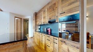 A modern kitchen with wooden cabinetry and black countertops. - Apartment in Ski In Ski Out Location (Veysonnaz)