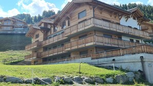 A multi-story wooden chalet with balconies, set against a backdrop of a clear sky and a hillside. - Apartment in Ski In Ski Out Location (Veysonnaz)