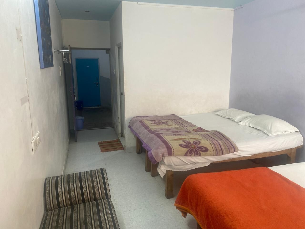 Una habitación pequeña y funcional con dos camas individuales, un banco y una puerta que da a un pasillo.