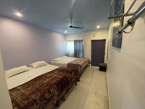 Quarto com duas camas, ventilador de teto, porta e uma pequena mesa.