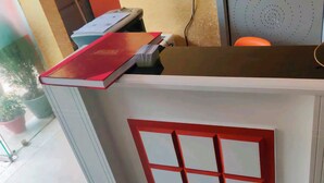 A reception desk with a red book on top, a printer, and a chair. - Hotel Ram Palace (New Delhi)