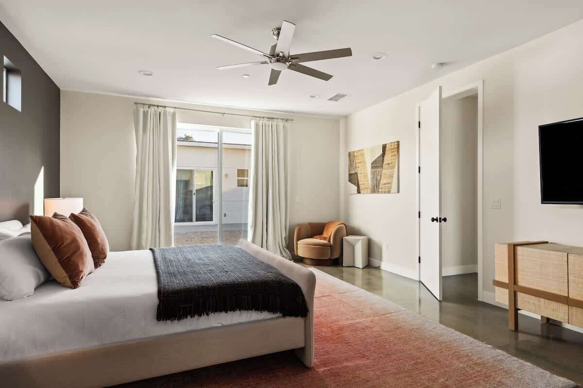 A modern bedroom with a large bed, a ceiling fan, a TV, and a sliding door leading to a balcony.