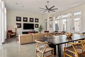 A modern living room with a large sofa, dining table, and chairs, a flat-screen TV, and artwork on the walls.