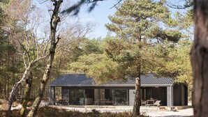 A modern cabin with a glass facade, surrounded by a forest.