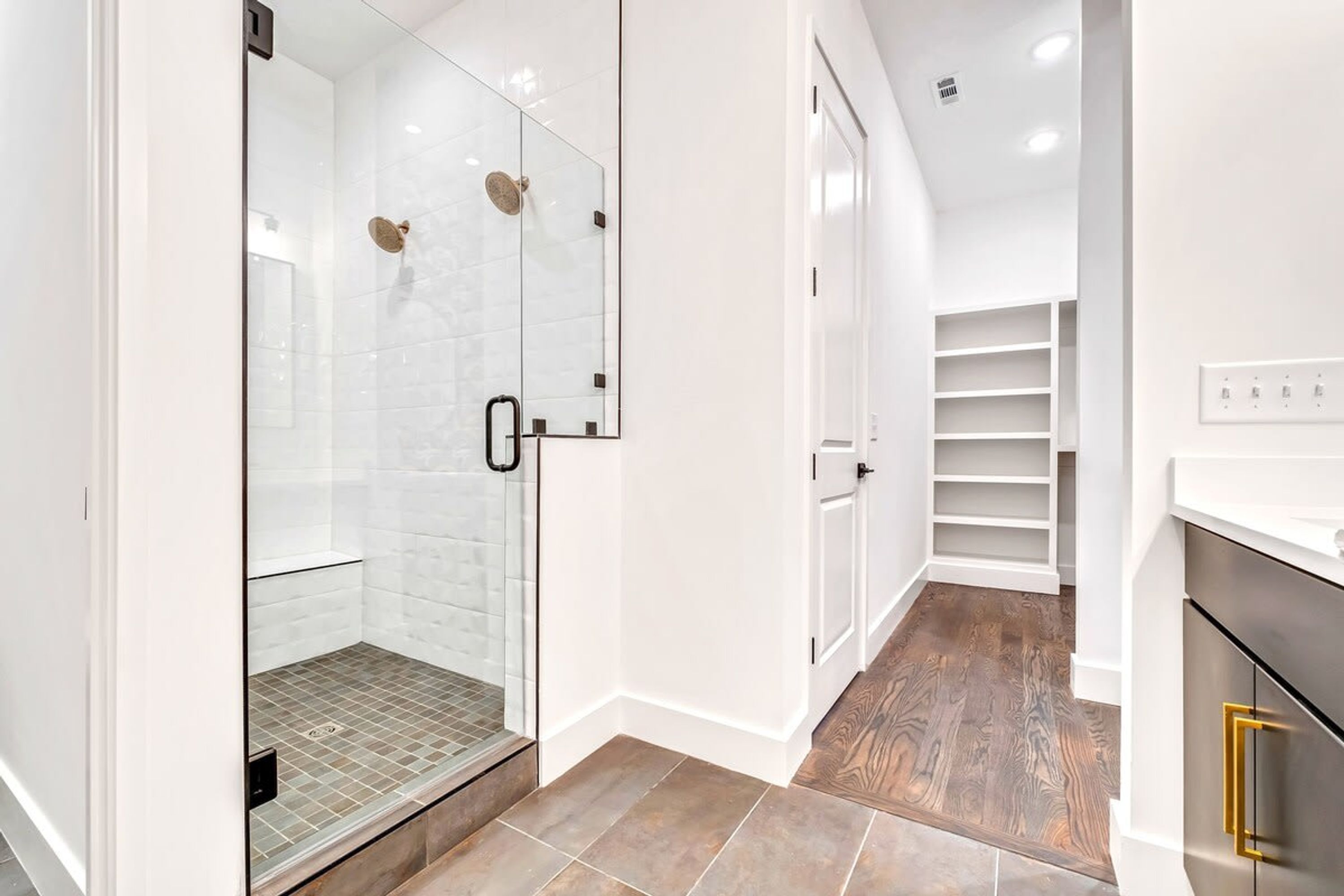 Un bagno moderno con doccia vetro, pareti piastrellate di bianco e pavimento in legno.