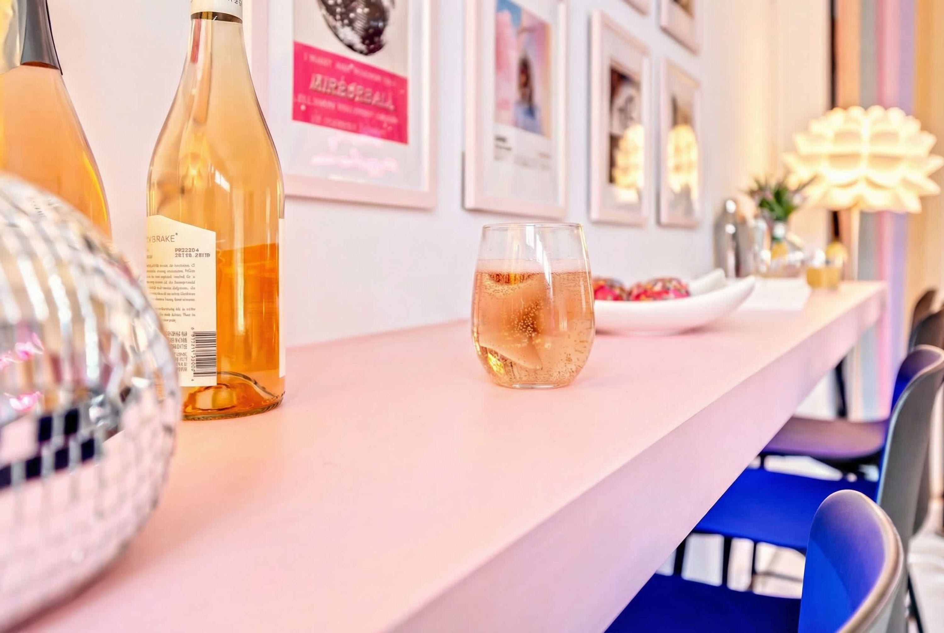 Een bar met flessen en glazen, een discobal en ingelijste foto's aan de muur.