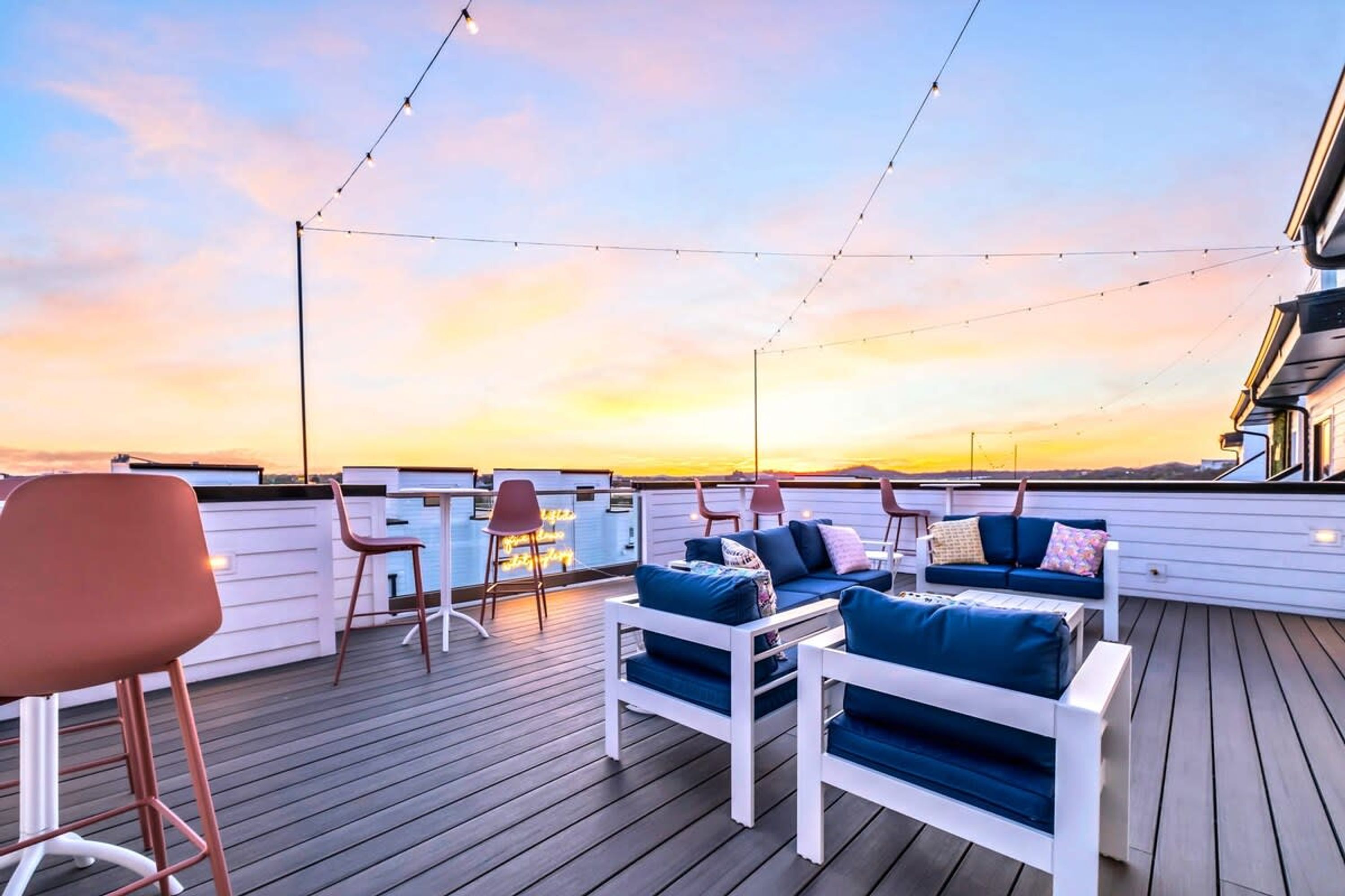 Une terrasse avec des sièges et des guirlandes lumineuses, offrant une vue sur le coucher du soleil.