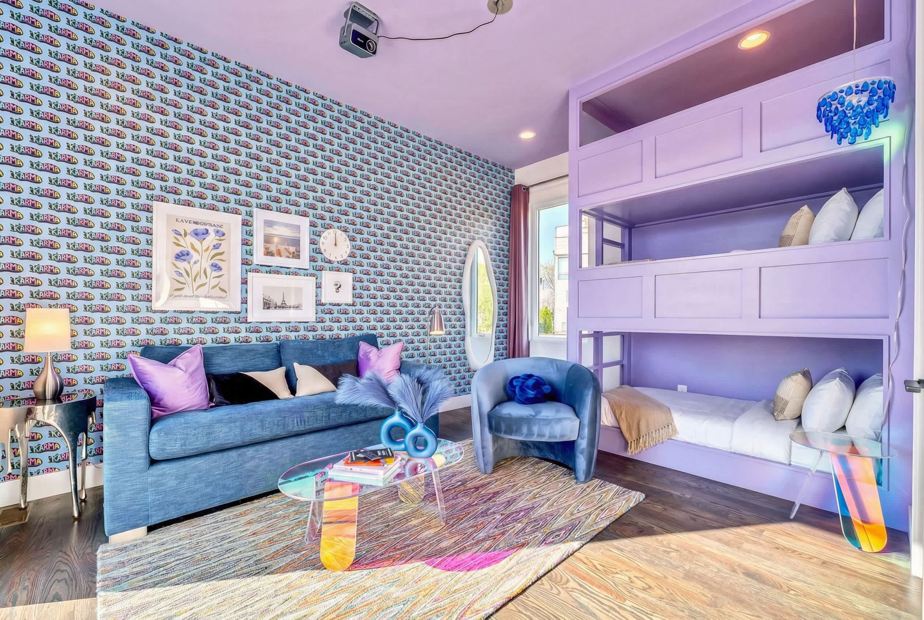 A modern living room with a patterned wall, a blue sofa, a glass coffee table, and a purple shelving unit.