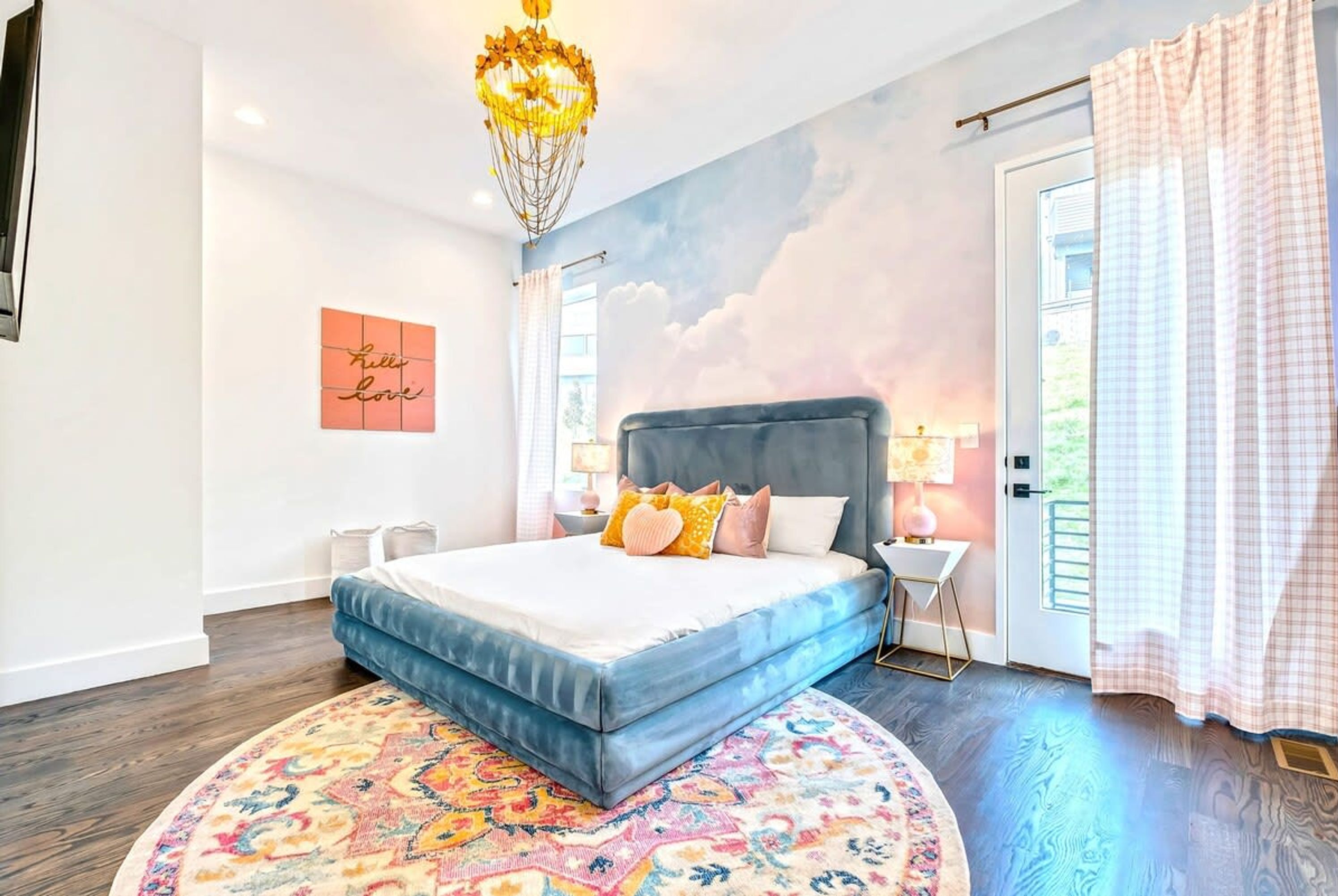 A bedroom with a bed, a chandelier, a wall mural, a window, and a door.