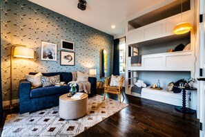 A living room with a blue sofa, a round coffee table, and a patterned rug. There are framed pictures on the wall and a mirror above the sofa. - Luxury Stay With Rooftop Views in Prime Location (Nashville)