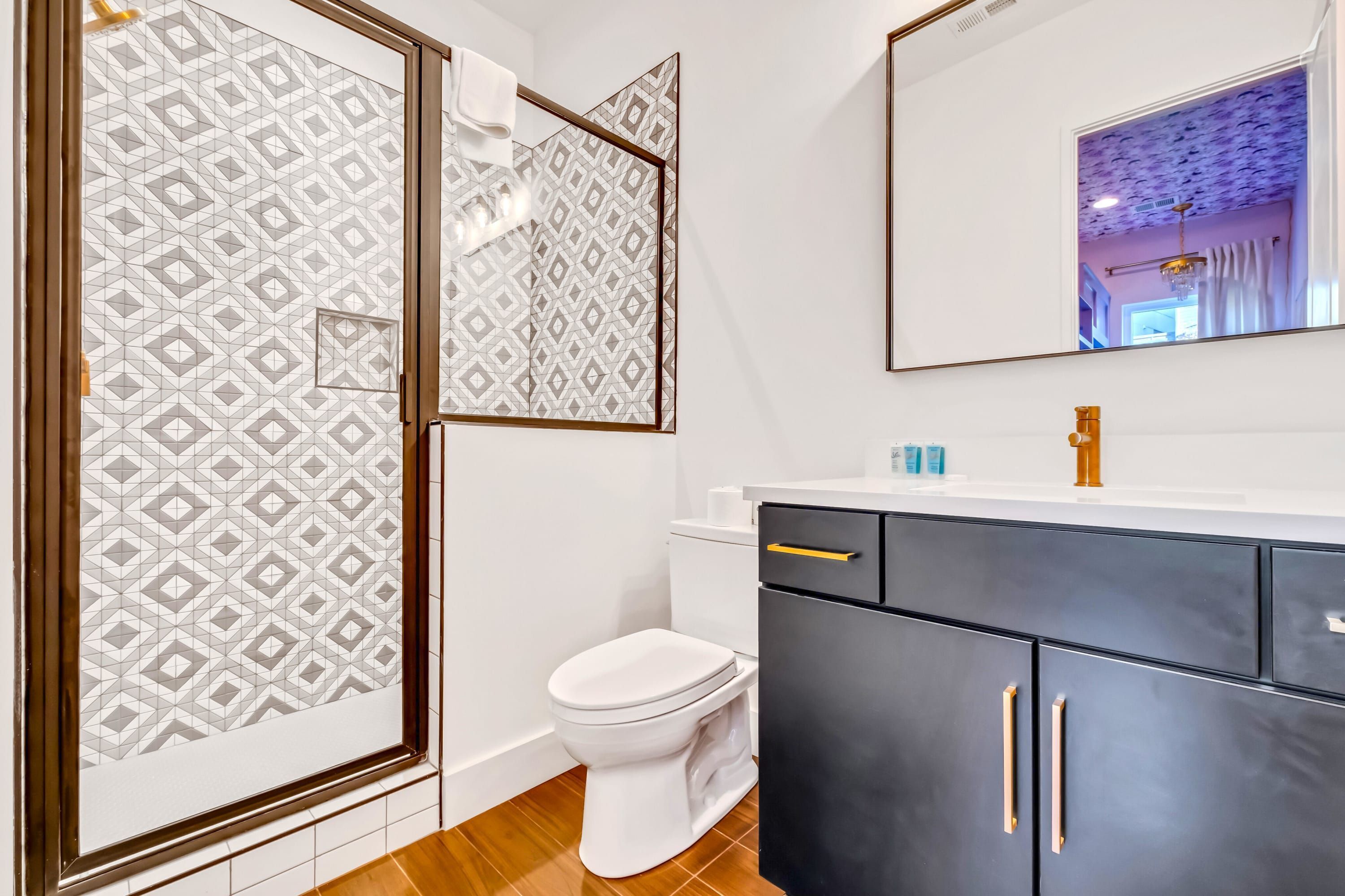 Un baño con inodoro blanco, un mueble negro con tiradores dorados y un espejo sobre el lavabo.