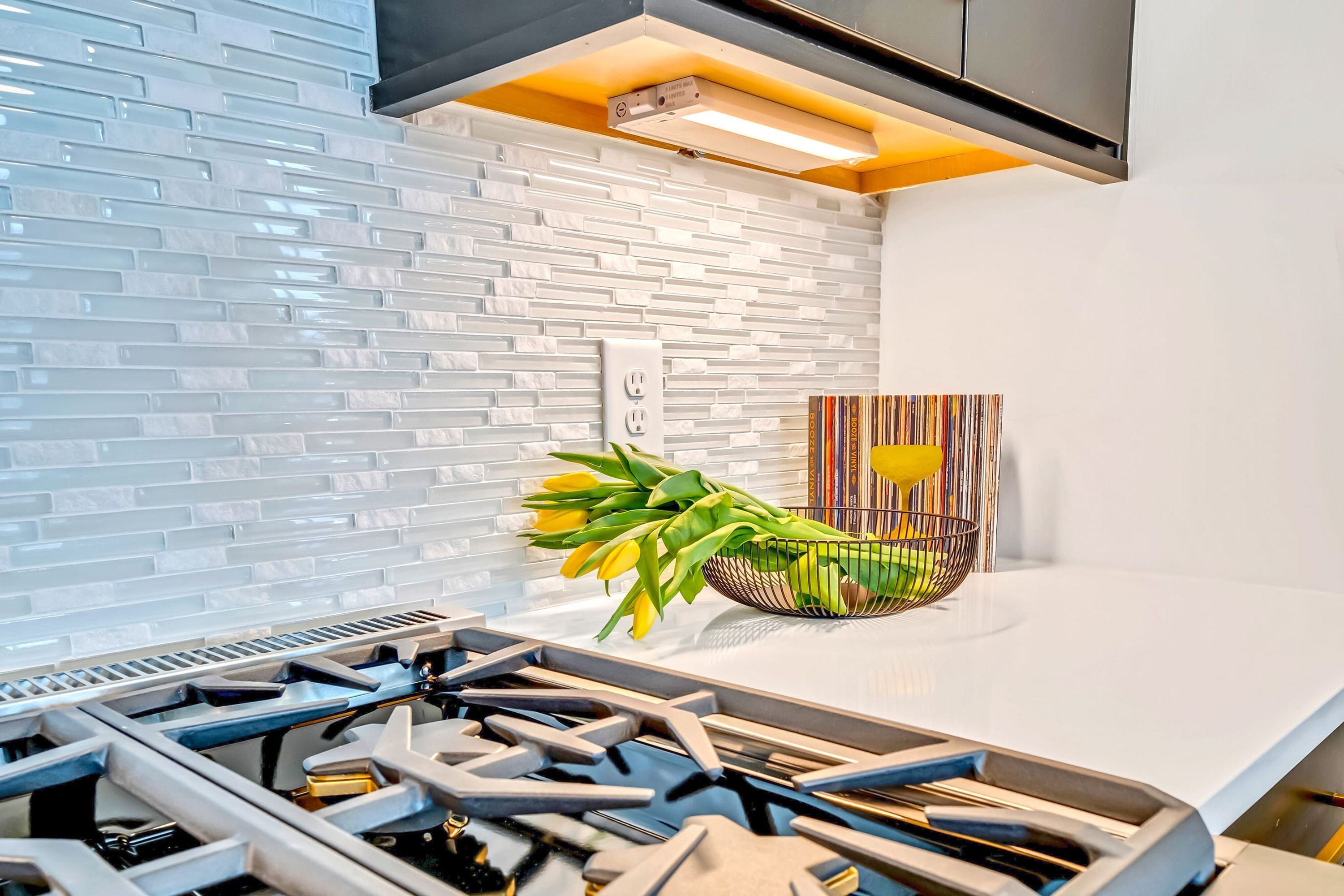 Une cuisine moderne avec un crédence carrelée de couleur blanche, une cuisinière à gaz et un bol décoratif rempli de fleurs jaunes.