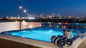 Un jacuzzi en la azotea con vista al horizonte urbano, una botella de champán y dos toallas enrolladas.