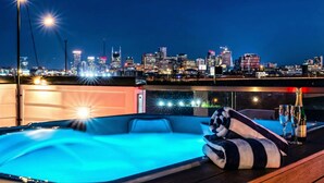 Un jacuzzi en la azotea con vista al horizonte urbano, balaustrada de cristal y una botella de champán cerca.