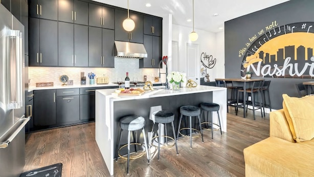 Una cocina moderna con armarios oscuros, una isla central con taburetes y un comedor con un mural de la ciudad.