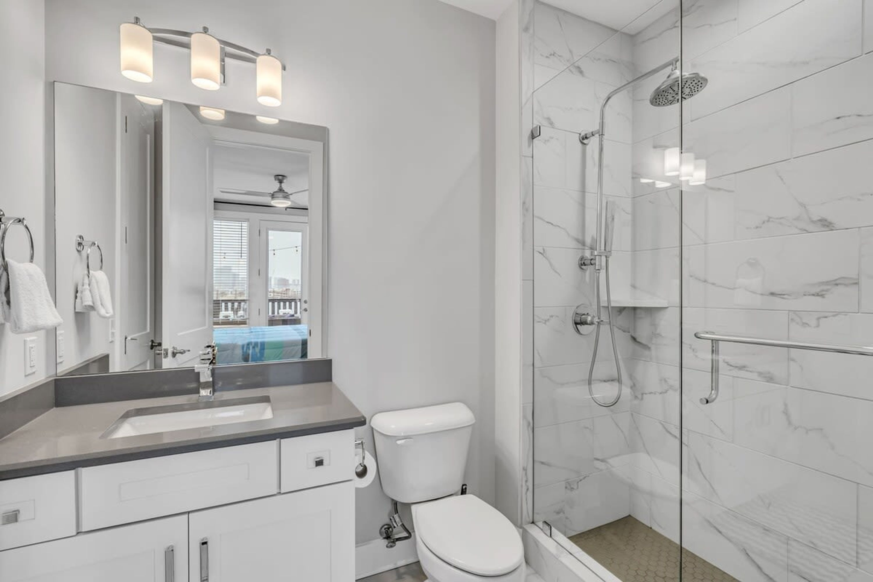 Un baño moderno con ducha de vidrio, inodoro blanco y tocador con espejo y lavamanos.
