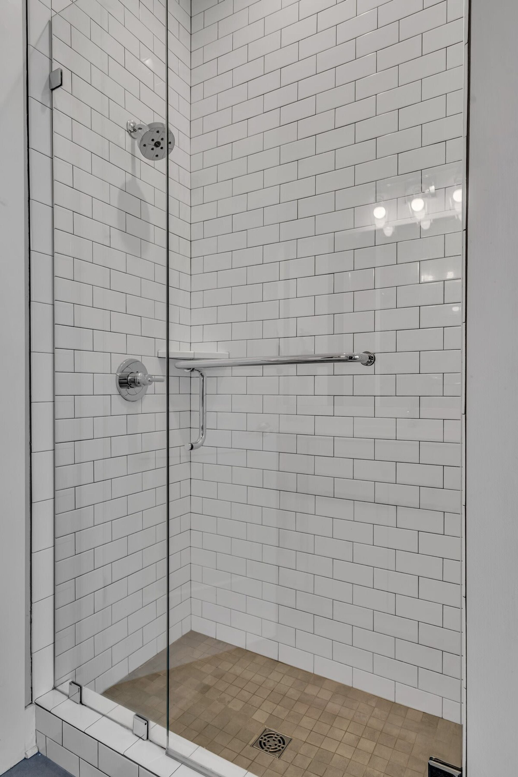 Ducha con mampara de vidrio, azulejos tipo metro blancos y ducha de cromo.