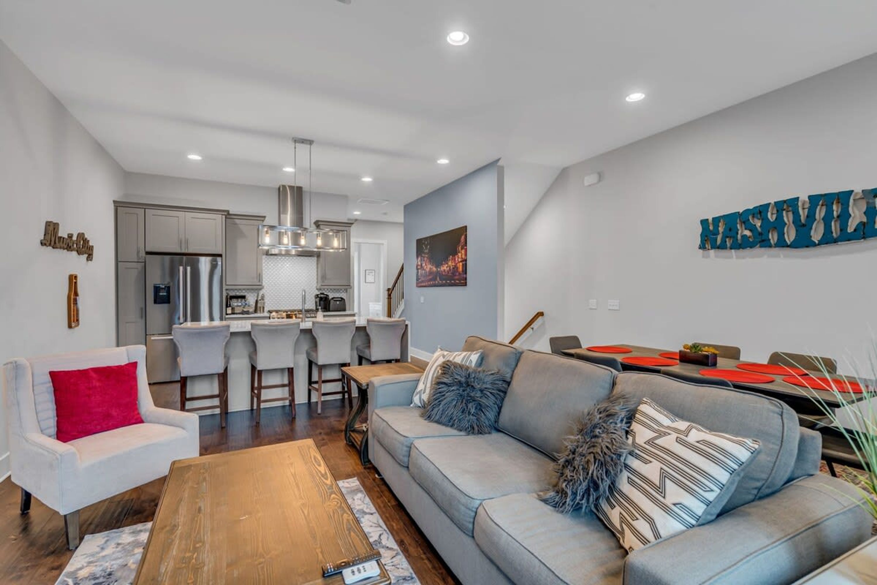 A modern living room with a grey sofa, wooden coffee table, and a dining area with red placemats.