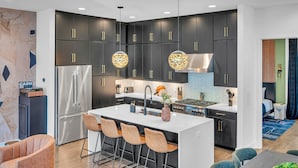 A modern kitchen with dark cabinets, stainless steel appliances, and a central island with bar stools. - Rooftop Hot Tub City Views Pac-man Pool Table (Nashville)
