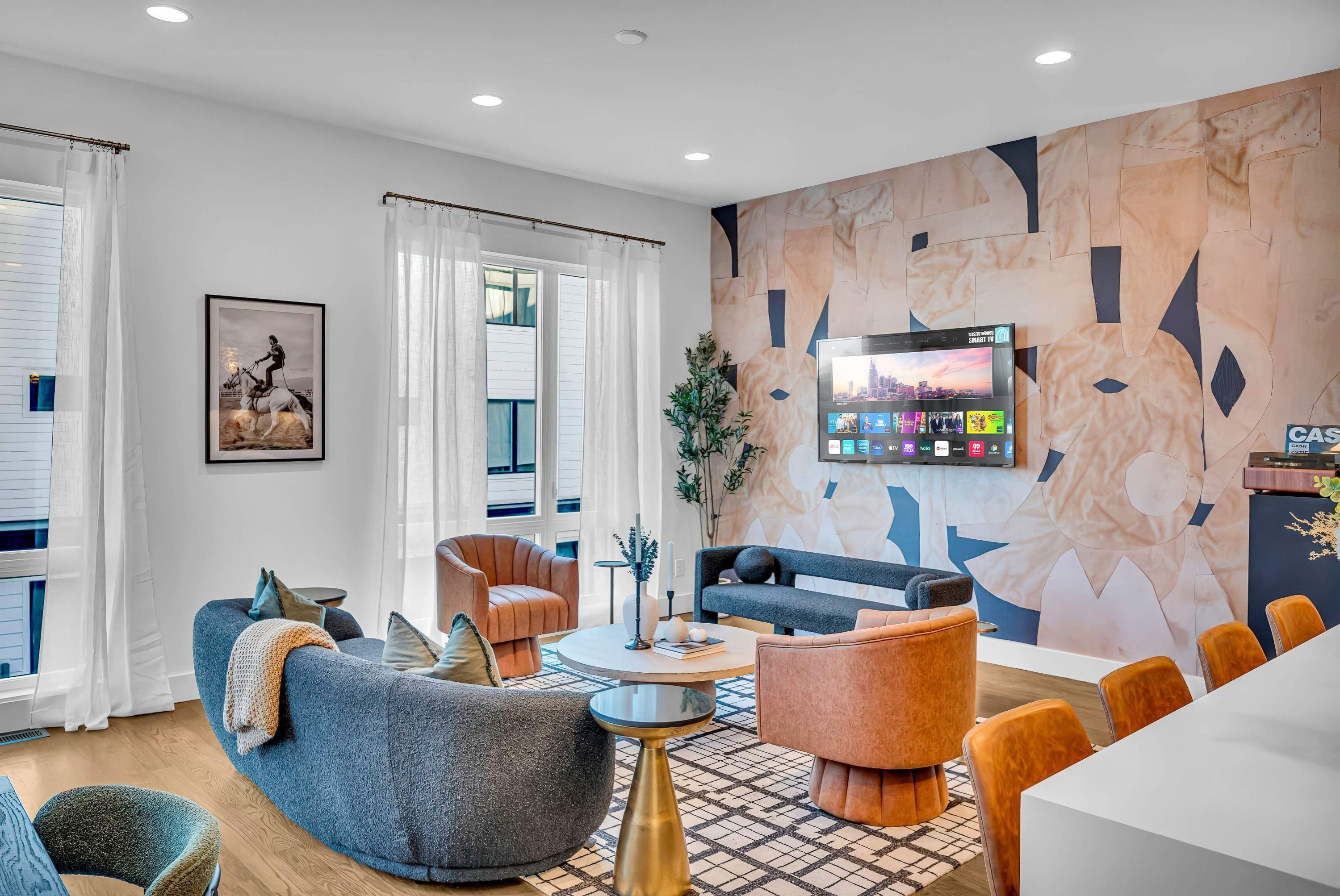 Un salon moderne avec un canapé, des fauteuils, une table basse et un téléviseur fixé au mur.