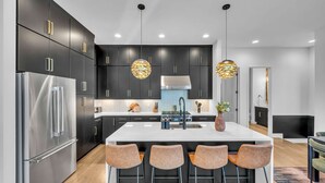 A modern kitchen with dark cabinetry, stainless steel appliances, and a central island with bar stools. - Rooftop Hot Tub City Views Pac-man Pool Table (Nashville)