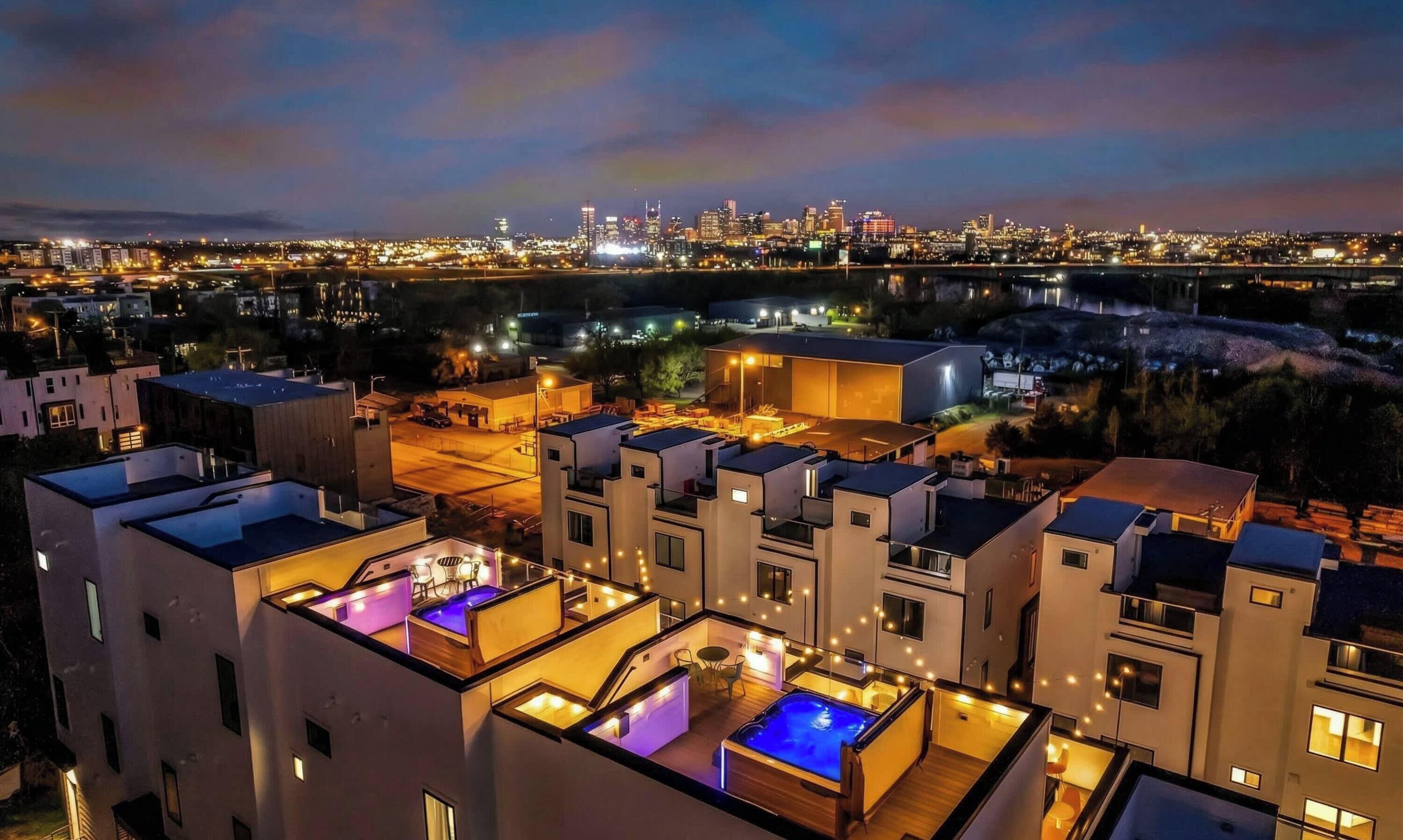 Un complexe résidentiel moderne doté de nombreuses terrasses sur le toit, comprenant des piscines et des espaces de détente en plein air, offrant une vue sur le paysage urbain au crépuscule.
