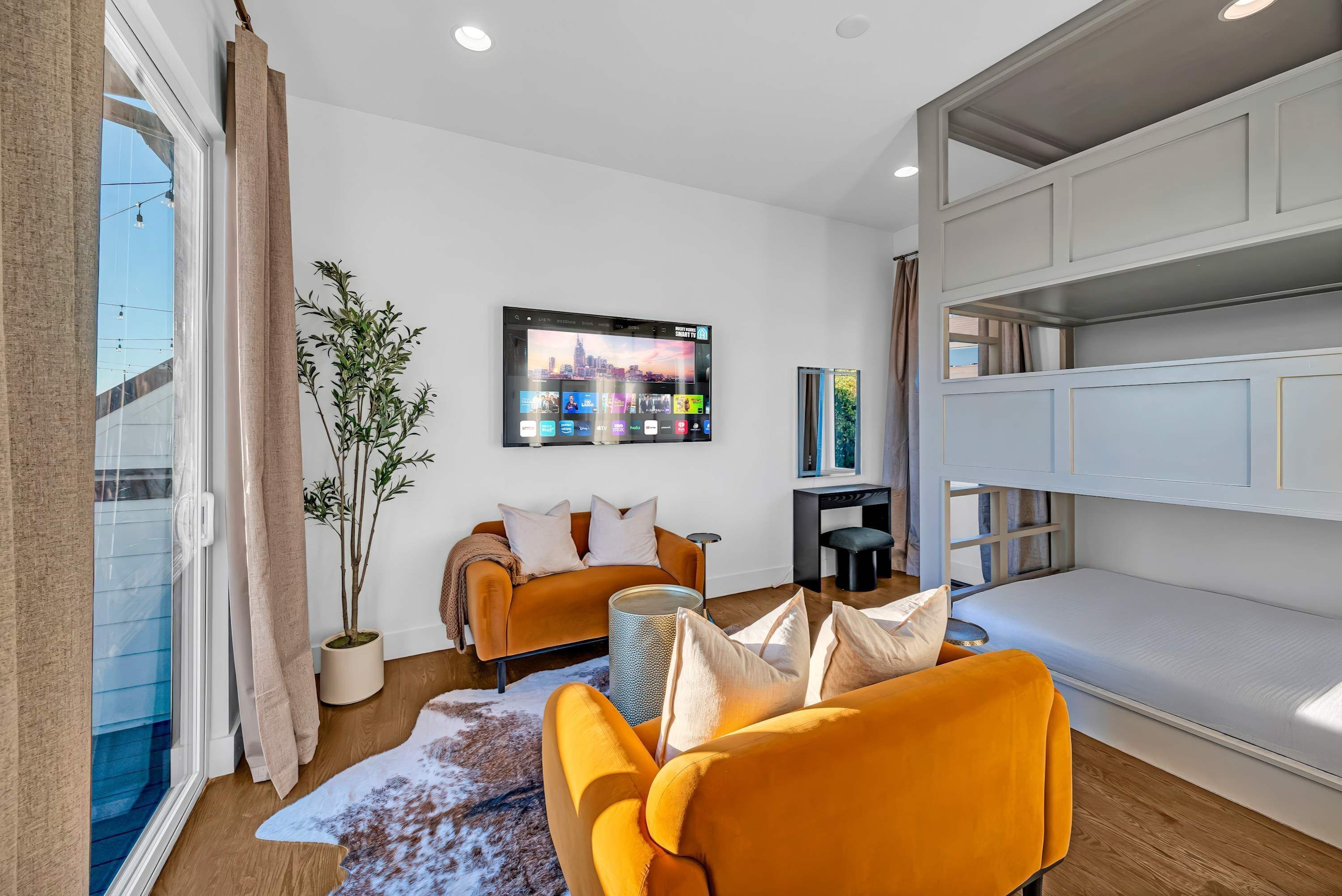 Ein modernes Wohnzimmer mit einer Couch, einem an der Wand befestigten Fernseher und einem Balkon mit Vorhängen.