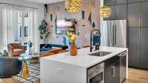 A modern kitchen with a central island, stainless steel appliances, and a large TV mounted on the wall. - Rooftop Hot Tub City Views Pac-man Pool Table (Nashville)