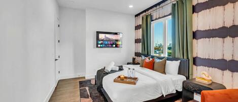 A modern bedroom with a bed, a TV mounted on the wall, a window with curtains, and a view of the cityscape.