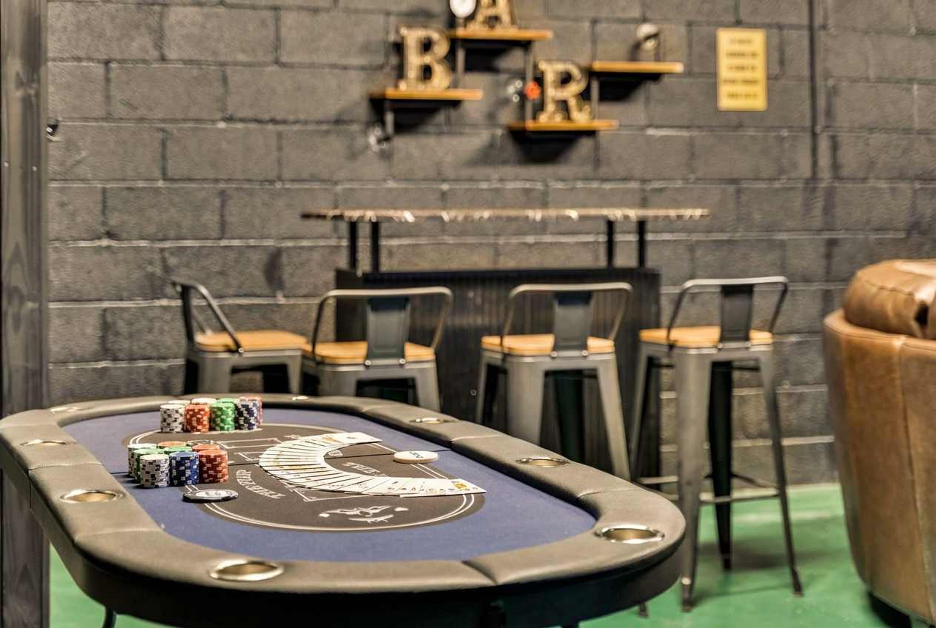 A pool table with chips and cards, a bar area with stools, and a brick wall.