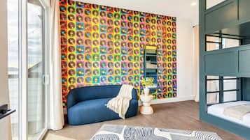 A room with a colorful vinyl record wall art, a blue sofa, a white bedside table, and a bunk bed.