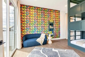 A room with a colorful vinyl record wall art, a blue sofa, a white bedside table, and a bunk bed. - New Hot Tub Rooftop Decks City Views Poker (Nashville)