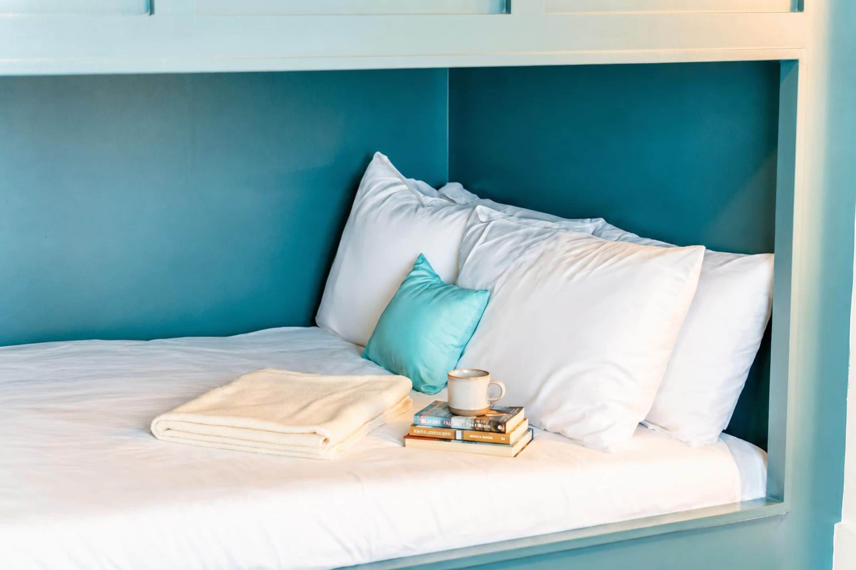 Una cama litera con ropa de cama blanca y una pared azul verdosa.