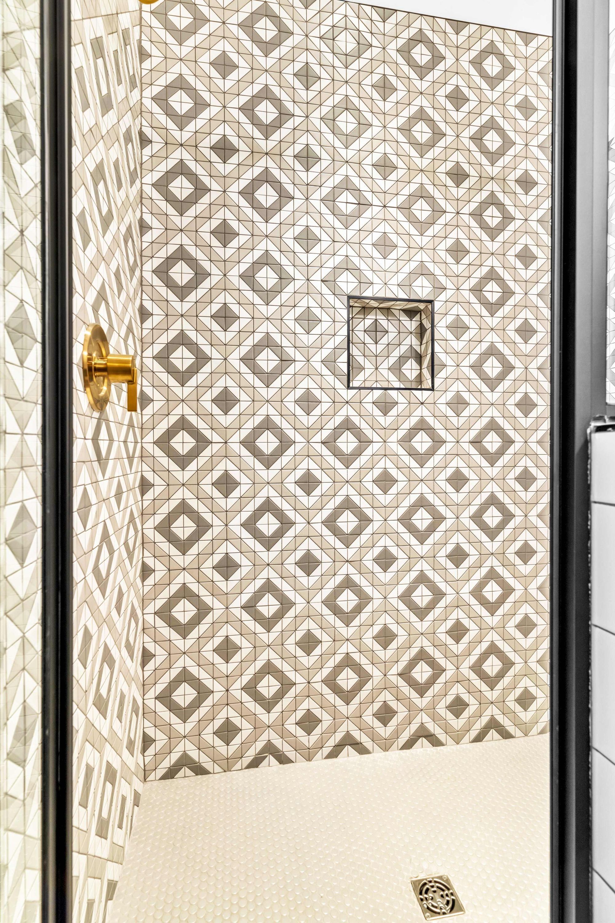Un baño con azulejos estampados, un grifo dorado y un suelo con textura.