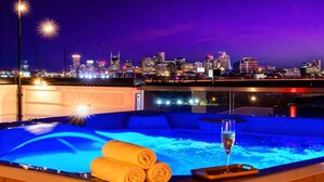 Ein Whirlpool mit Handtüchern und einem Glas Champagner mit Blick auf eine beleuchtete Stadtlandschaft in der Nacht.