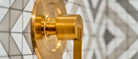 A wall-mounted, gold-colored, cylindrical object with a lever, set against a geometric patterned background.