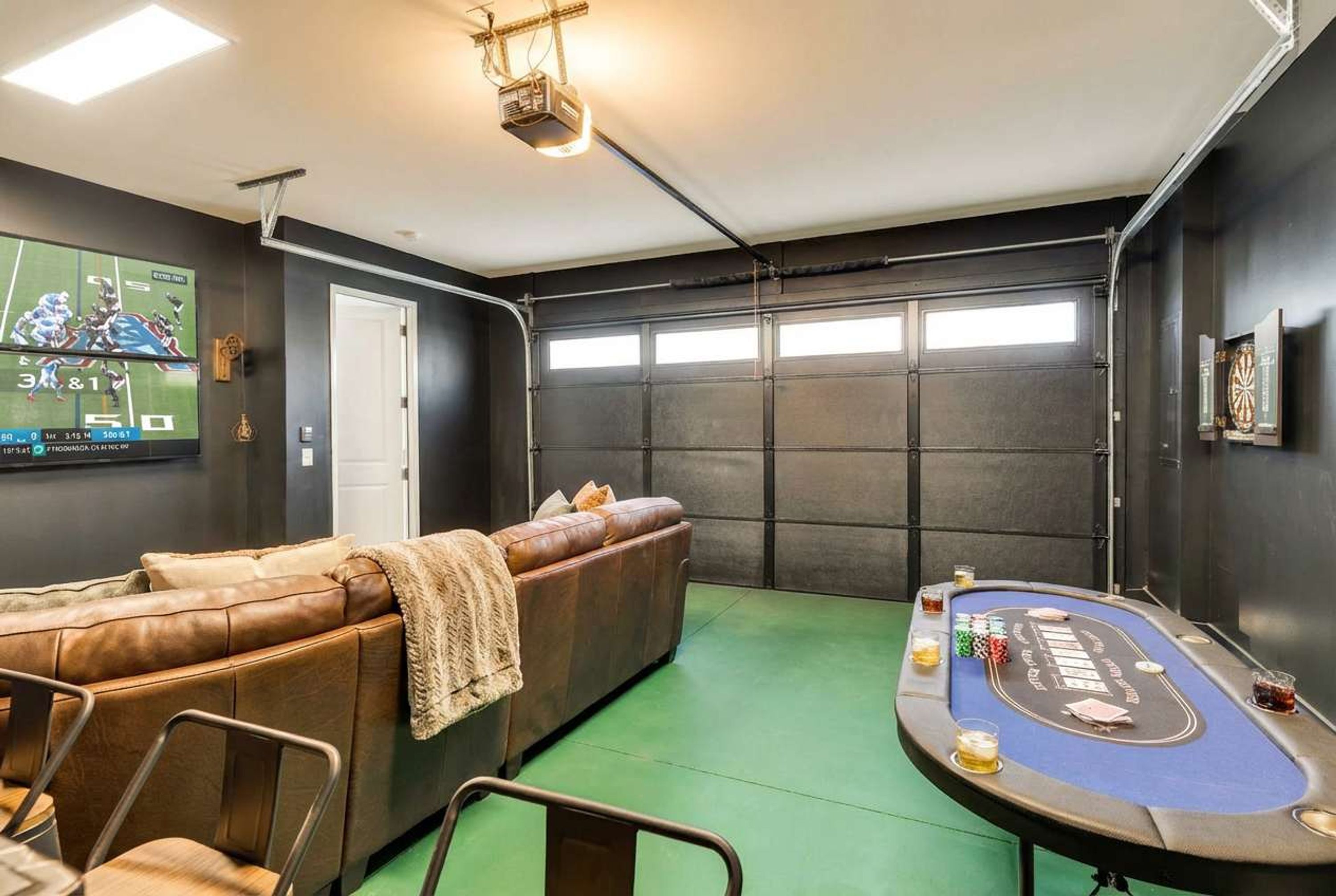 A room with a pool table, a leather couch, and a television displaying a sports game.